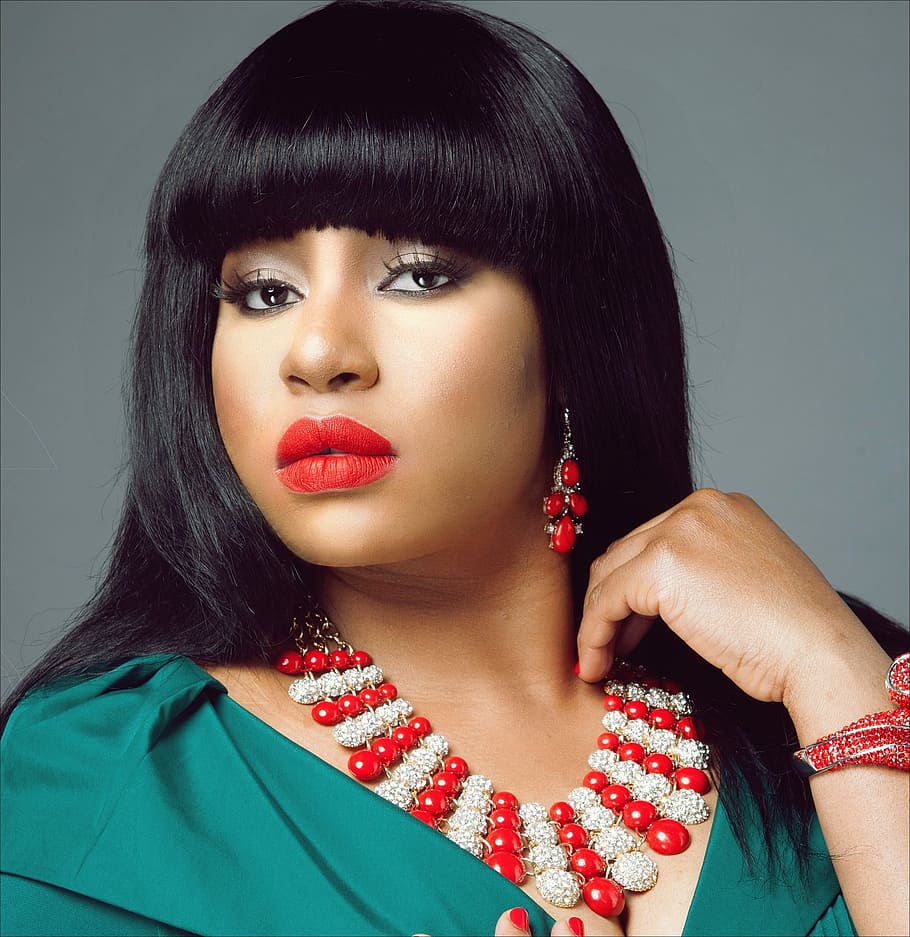 woman wearing blue shirt, red beaded bib necklace, red lipstick and dangling earrings