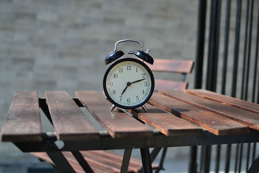 black steel alarm clock on top of brown table, selective focus photography of twin bell clock
