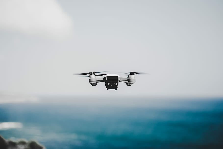 white quadcopter hovering near body of water, white and black drone hovering on air