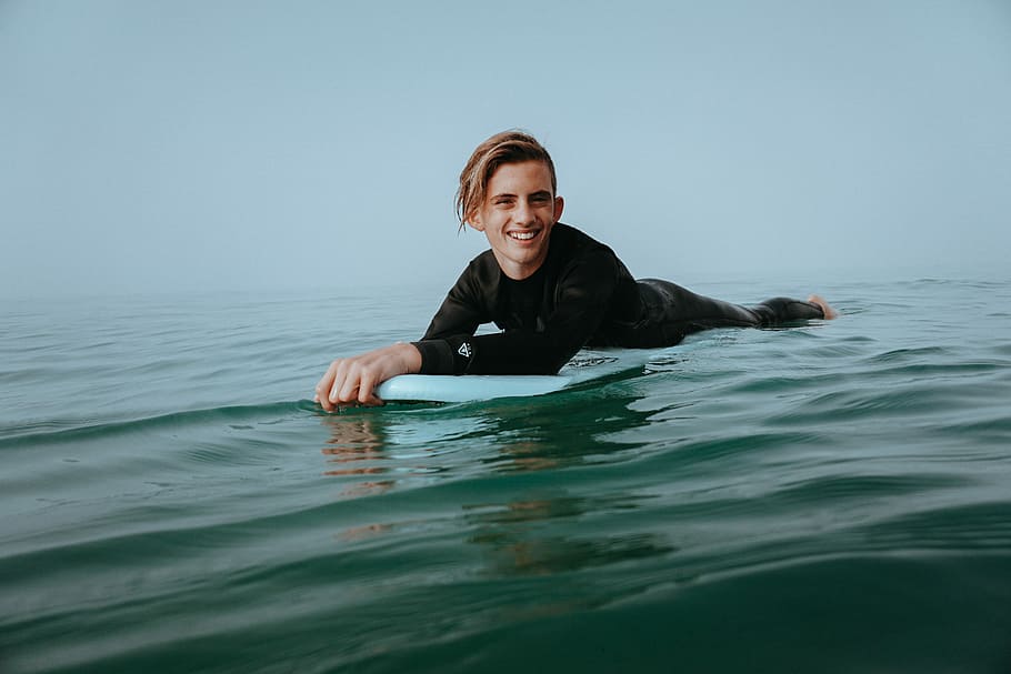man holding knee board on body of water, smiling man riding on white surfboard HD wallpaper