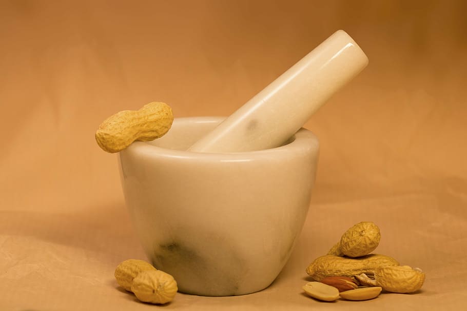 white ceramic mortar and pestle with brown nuts, peanuts, peanut butter