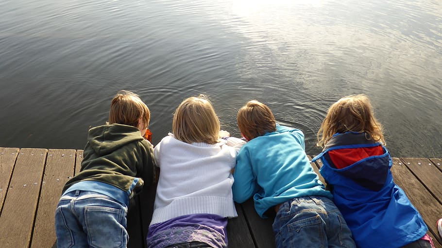 four toddlers in assorted-color jackets planking on brown wooden dock near water during daytime HD wallpaper