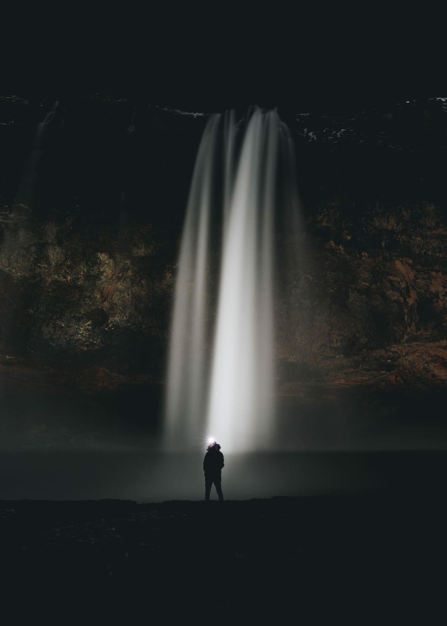 man standing in front of waterfalls during nighttime, person standing near waterfalls HD wallpaper