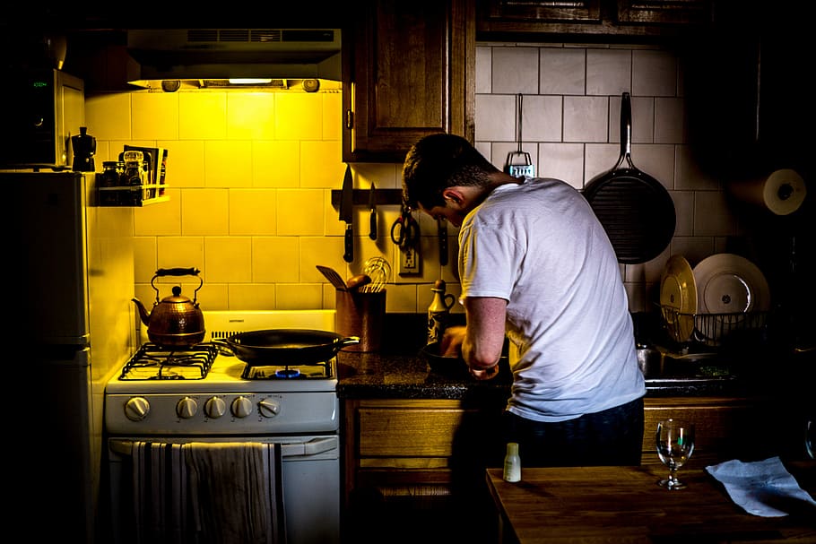 man standing beside range oven, lowlight photography of man in white shirt standing in front of kitchen cabinet beside gas range oven HD wallpaper