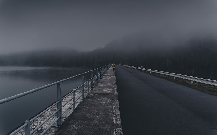 person wearing orange jacket walking on road near body of water HD wallpaper