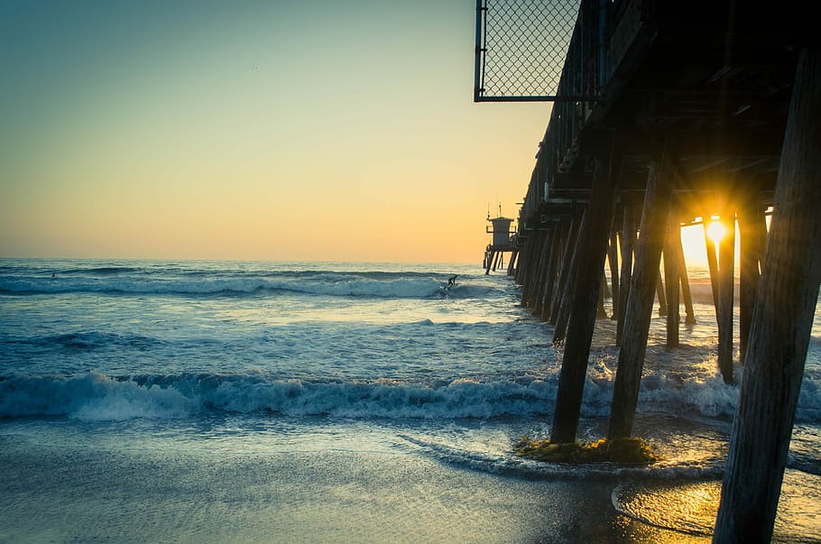 brown wooden sea dock during sunset, landscape photography of sea dock with sun rays HD wallpaper