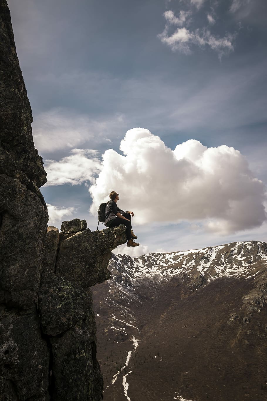 man sitting on mountain edge while looking at the sky, person wearing gray shirt seating on cliff during daytime