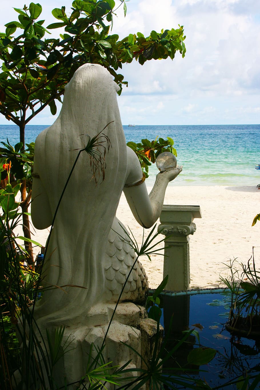 mermaid statuette facing body of water, crystal ball, sea, sand