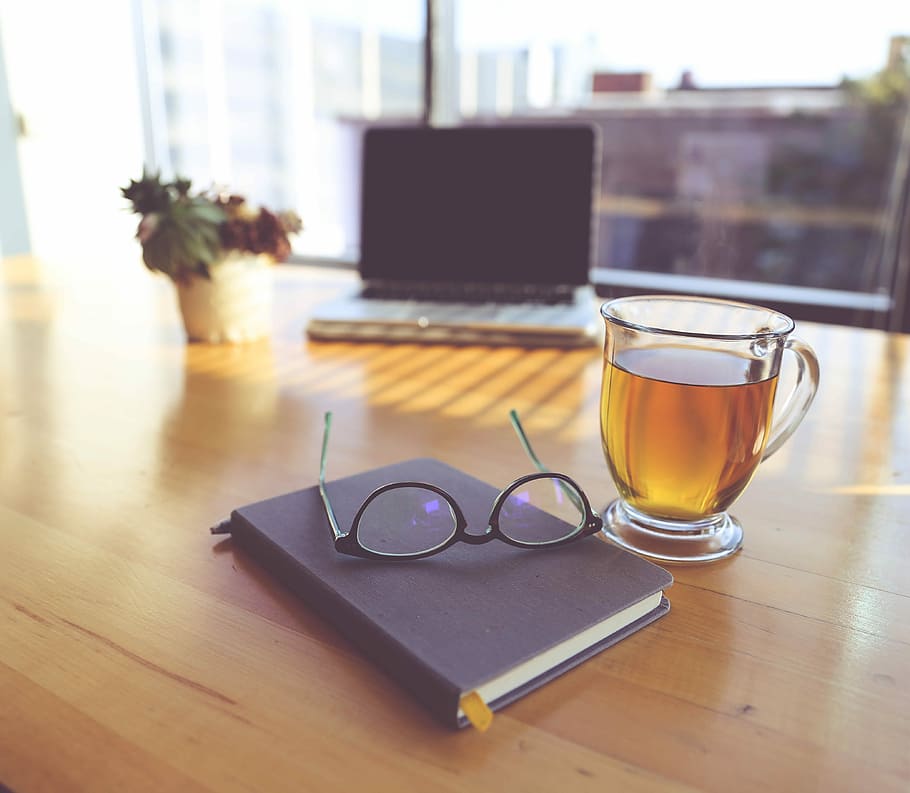 clear eyeglasses on top of black book beside clear glass mug, clear glass teacup filled with brown tea beside eyeglasses on top of brown wooden table HD wallpaper