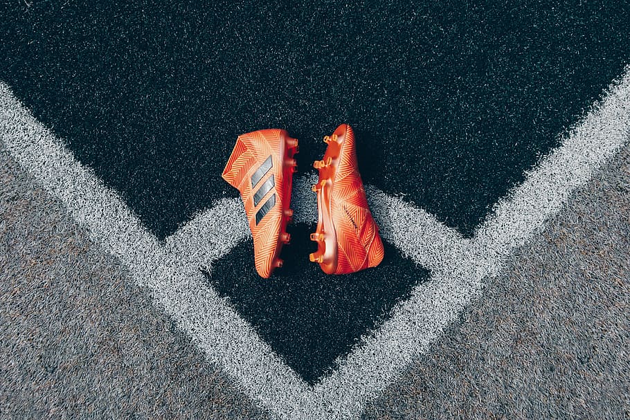 pair of orange adidas cleats on gray surface, pair of orange adidas soccer cleats on game field