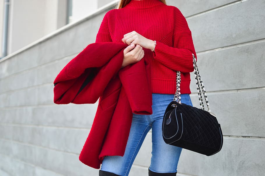 woman in red sweater beside white wall, woman carrying black shoulder bag