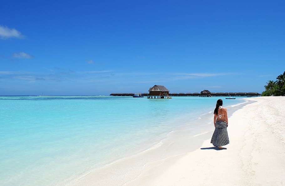 woman walking in seashore under blue sky at daytime, maldives