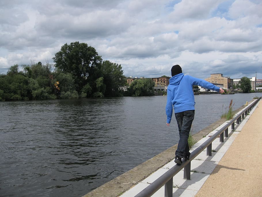 man walking while balancing on railing beside river at daytime HD wallpaper