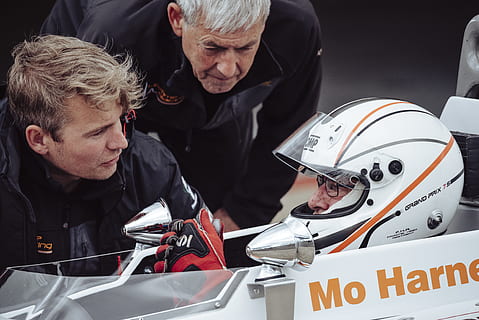 man in black jacket talking to the a wearing white full-face helmet during daytime, selective focus photography of two men standing beside man in white F1 race car at daytime HD wallpaper