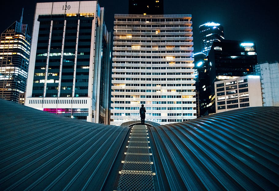 person standing on building roof with city buildings on background, person walking on green metal road HD wallpaper