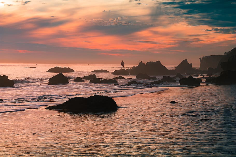 silhouette person standing on seashore rock during daytime, man standing on rock during sunset HD wallpaper