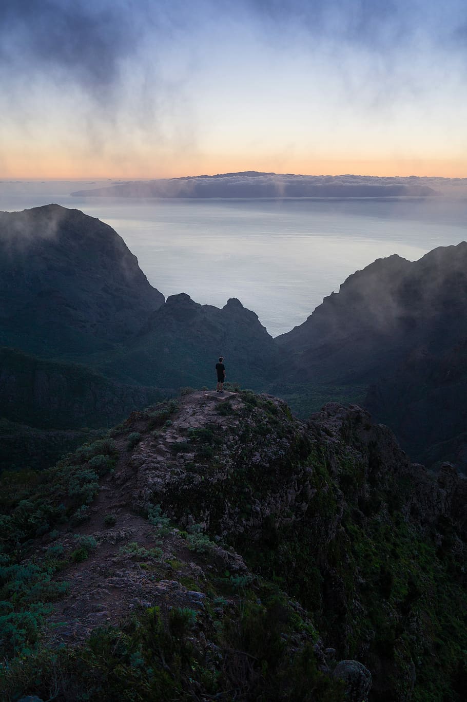 man in black t-shirt and black shorts standing near mountain beside body of water during day time HD wallpaper