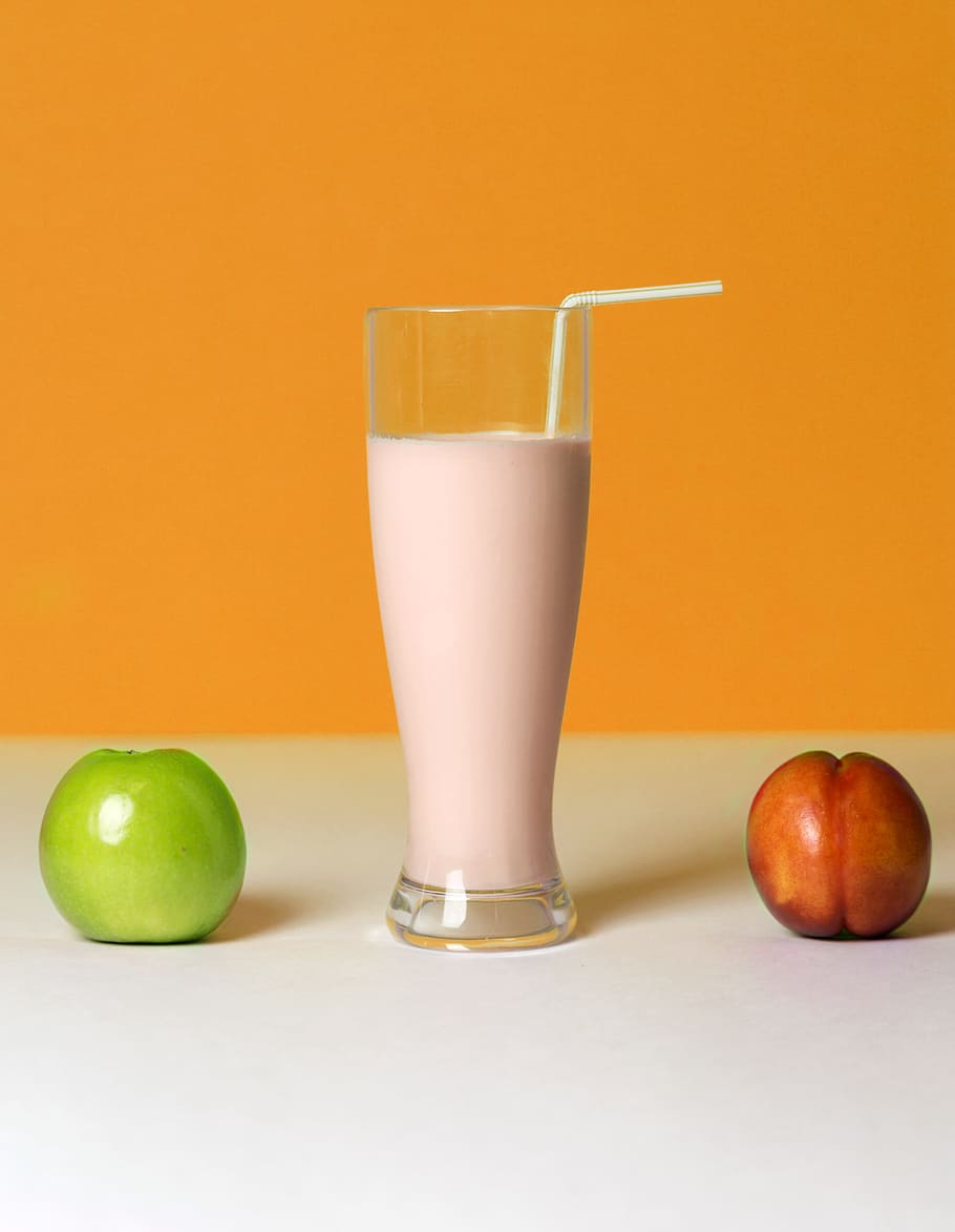 juice drink inside clear pilsner glass beside two red and green apples HD wallpaper