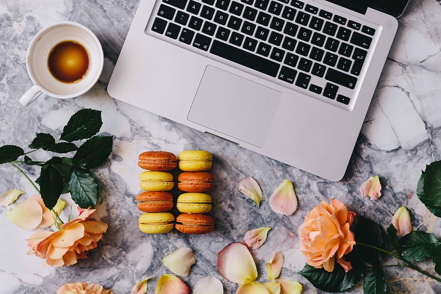 Overhead view of macarons on a marble slab, roses, workspace