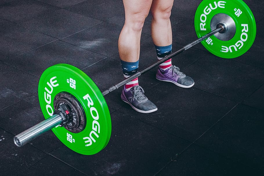 person standing in front of gray and green barbell, green-and-gray Rogue barbells