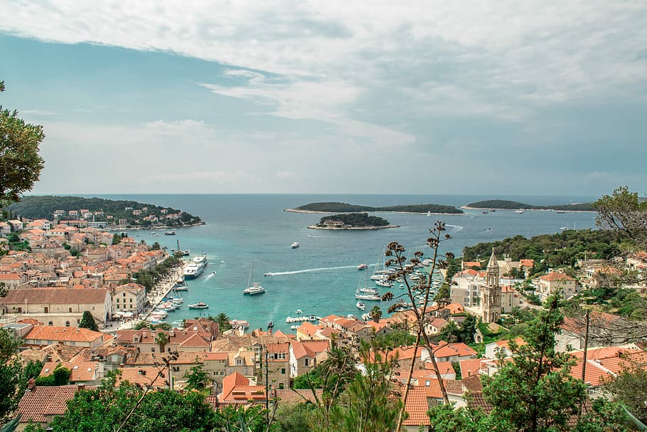 bird's eye view of village seashore, buildings by dock while boat at sea under white skies during daytime HD wallpaper