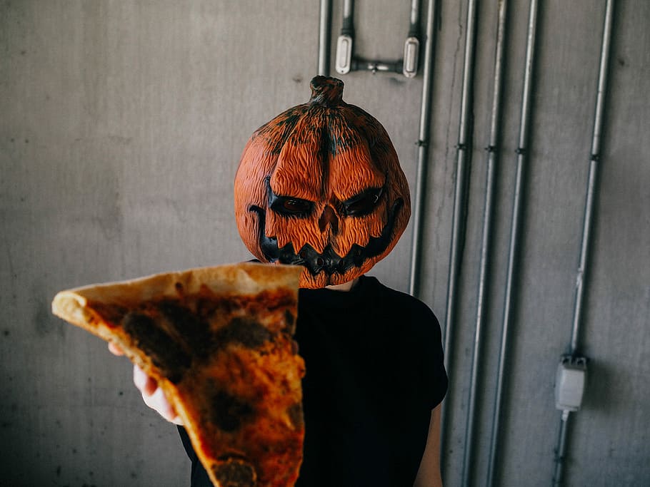 man wearing Jack'-o-lantern mask holding sliced pizza, person with pumpkin mask holding pizza slice, HD wallpaper