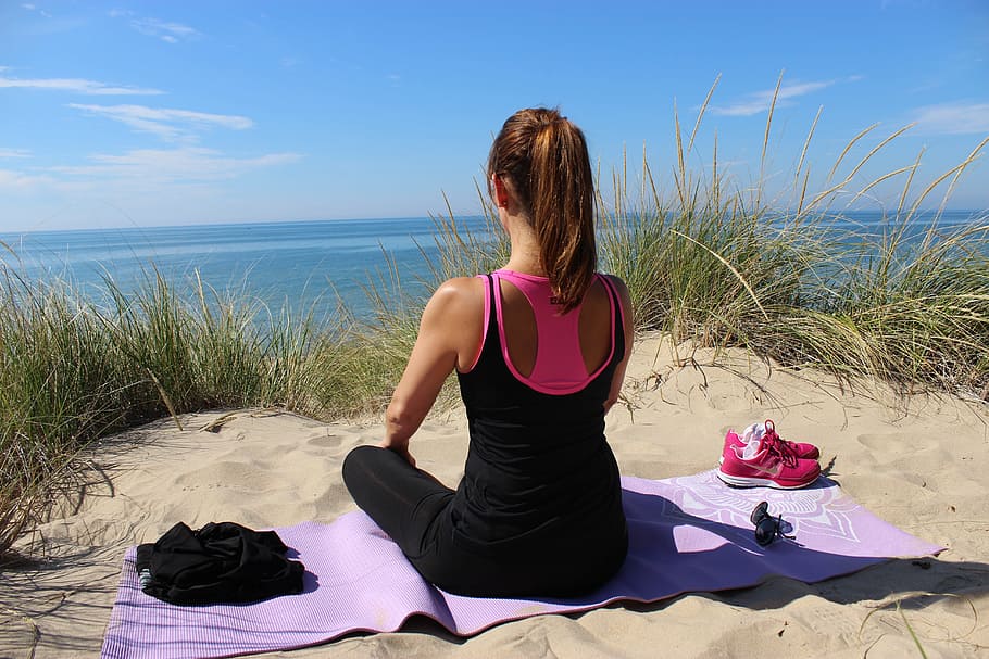 woman in black sleeveless top and black leggings sitting of purple yoga mat on sand near body of water during daytime HD wallpaper