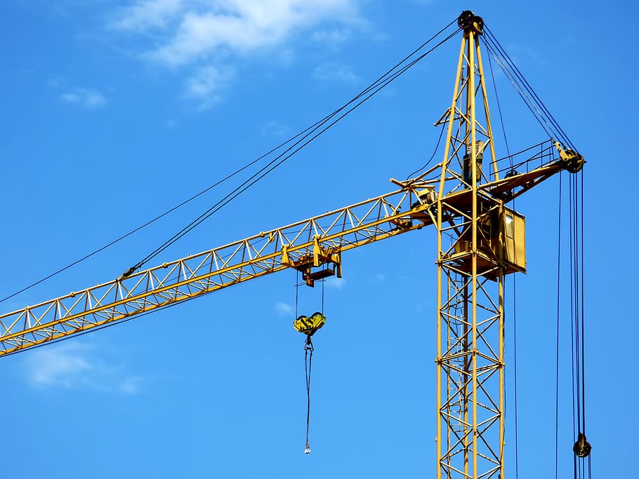 close-up photography of yellow tower crane during daytime, blue sky
