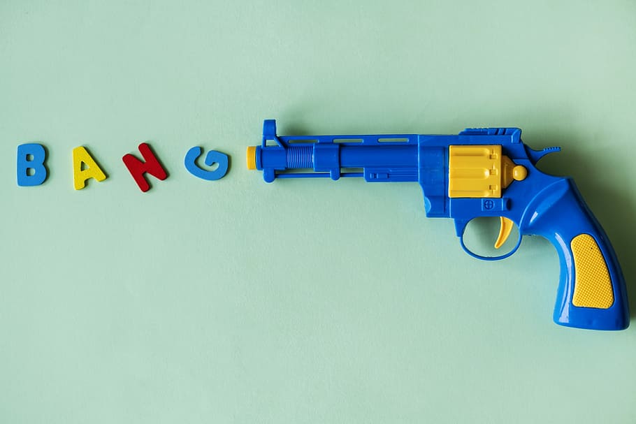 blue and yellow plastic revolver toy, arms, background, bang