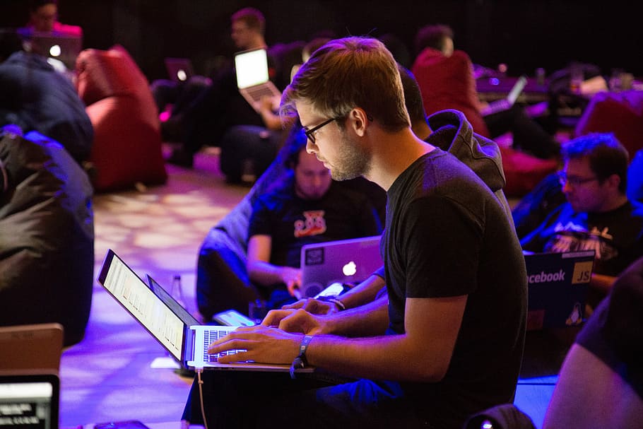 man using laptop in front of brown chair, man in black crew-neck t-shirt and black pants using laptop during nighttime HD wallpaper