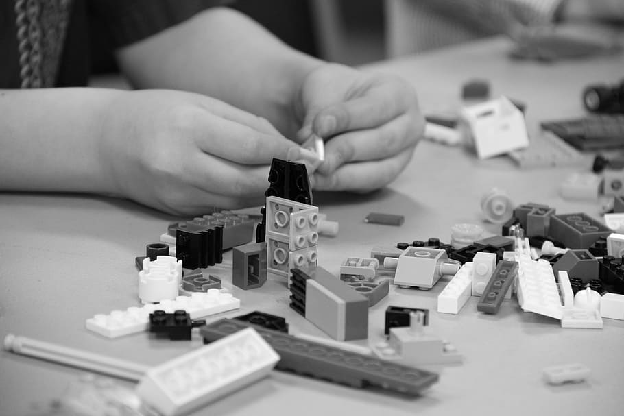 grayscale photo of person playing Lego pieces, toy, building