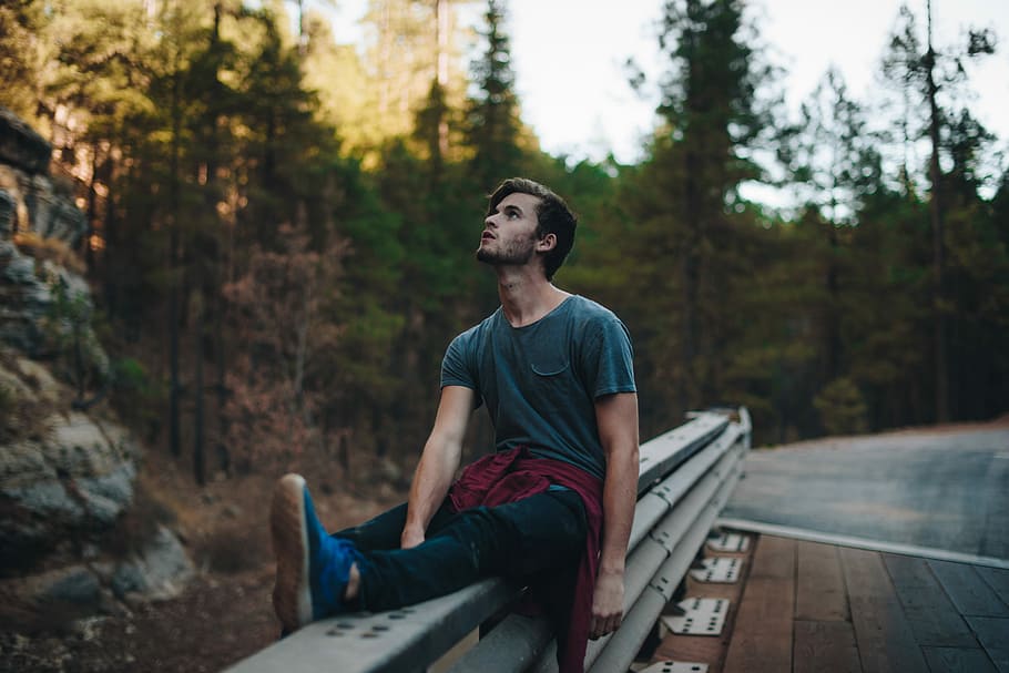man sitting on rails looking up during daytime, selective focus photography of man sitting on gray metal railings HD wallpaper