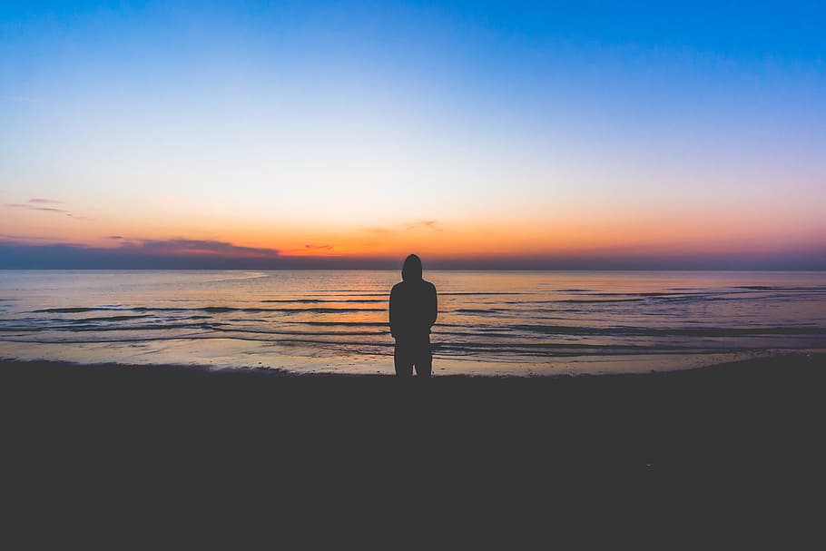 silhouette of person standing near sea during golden hour, silhouette of man wearing hoodie on seashore painting