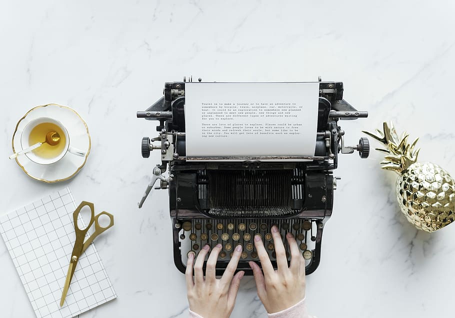 person typing on black typewriter with brown scissors beside and white cup HD wallpaper