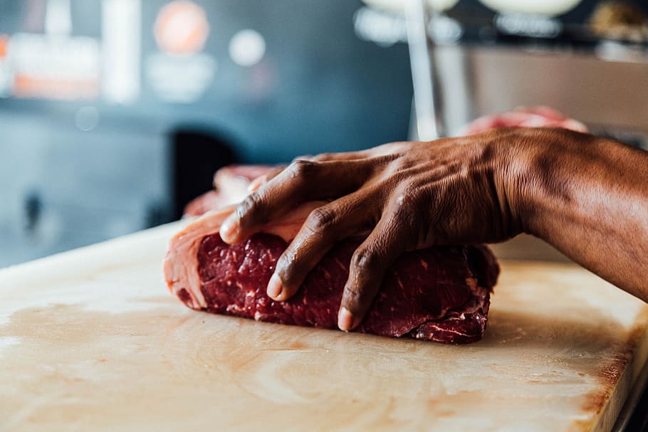 A butcher holding a piece of meat in his hand in Boca del Río, selective focus photography of person holding piece of meat placed on beige wooden board HD wallpaper