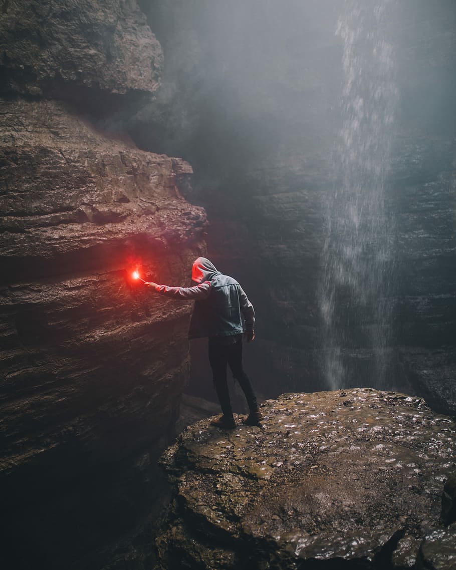 You’re a wizard harry, man holding red light inside cave beside waterfall