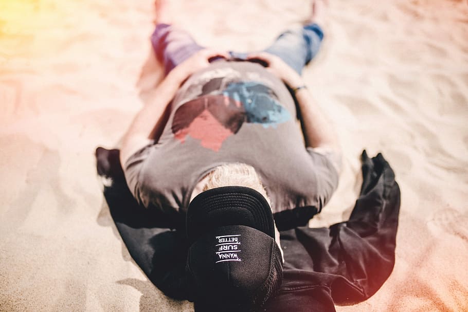 man in gray shirt lying on sand, man in brown and black cap, basecap HD wallpaper
