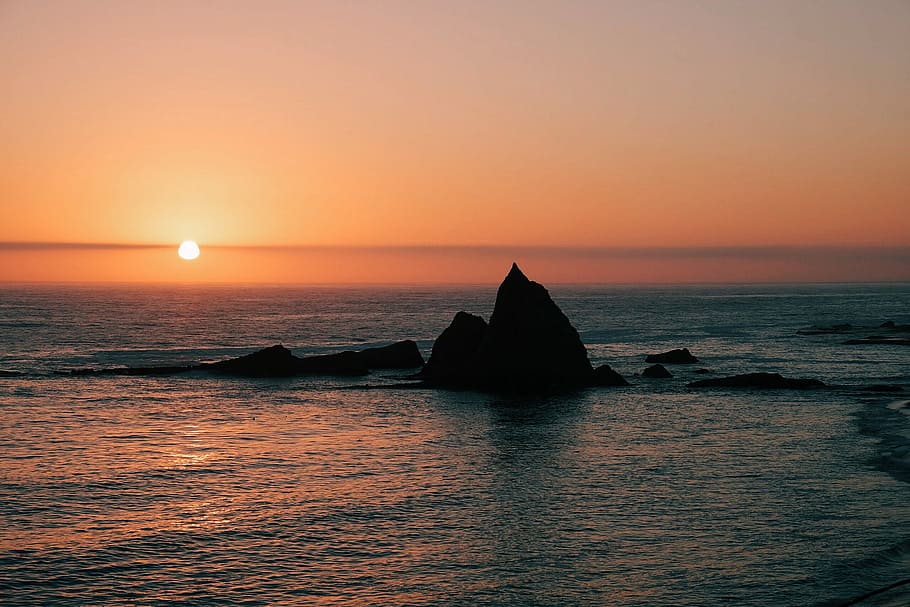 silhouette of rock formation surrounded by body of water at sunset, rule of thirds photography of orange sunset HD wallpaper