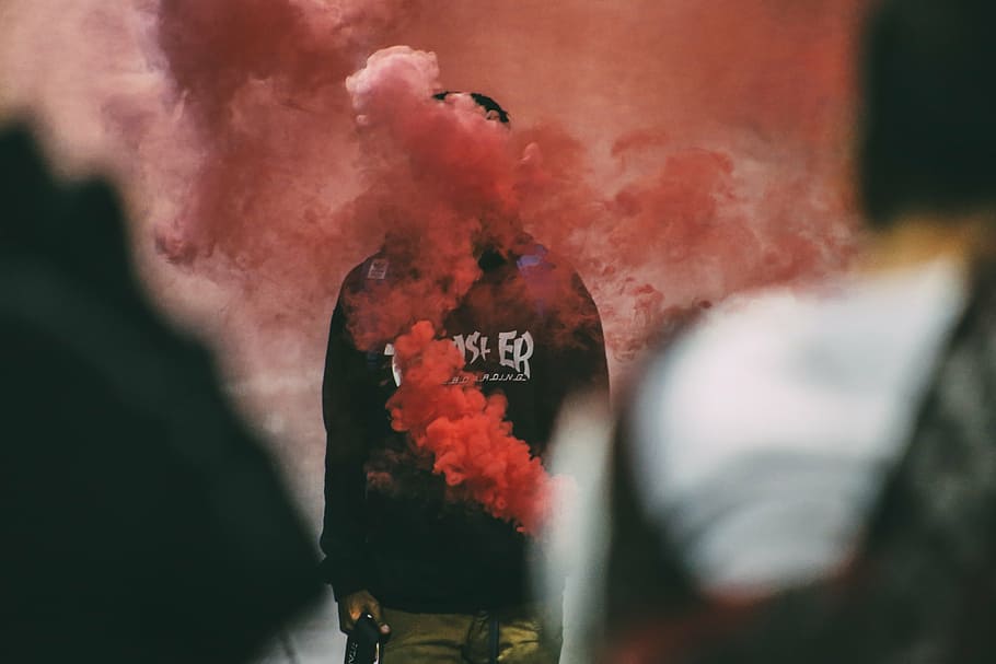 person wearing black Trasher shirt covered with pink smoke at daytime HD wallpaper