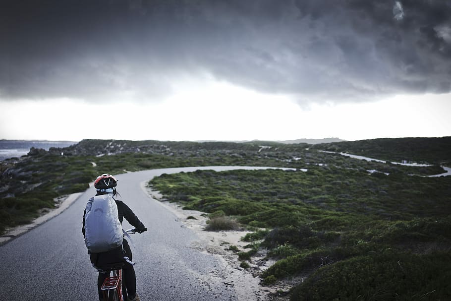 person riding bicycle near grass, person riding bicycle on black road under cloudy sky during daytime HD wallpaper