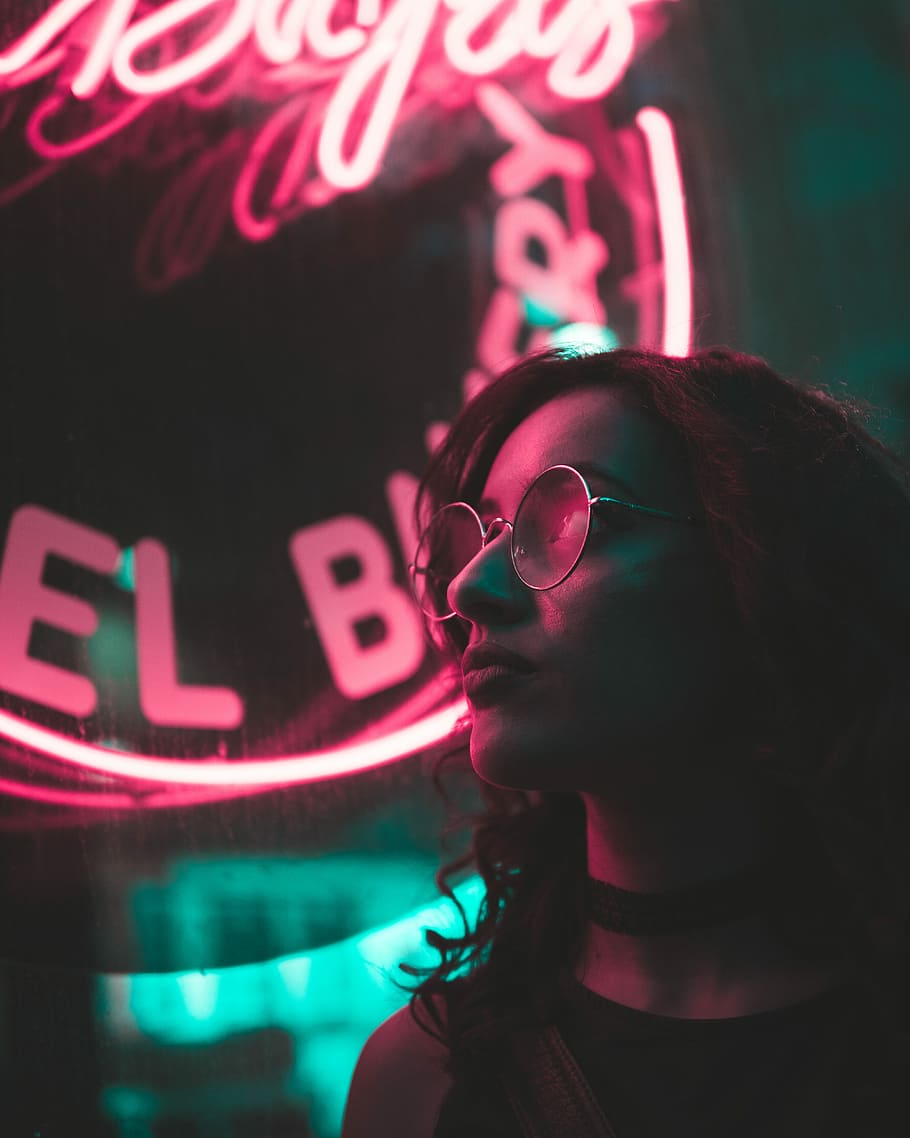 selective focus photo of woman with neon light signage background, woman standing near the red neon light during night time