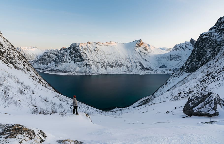 man standing on snow path, person standing near mountain peak and body of water HD wallpaper