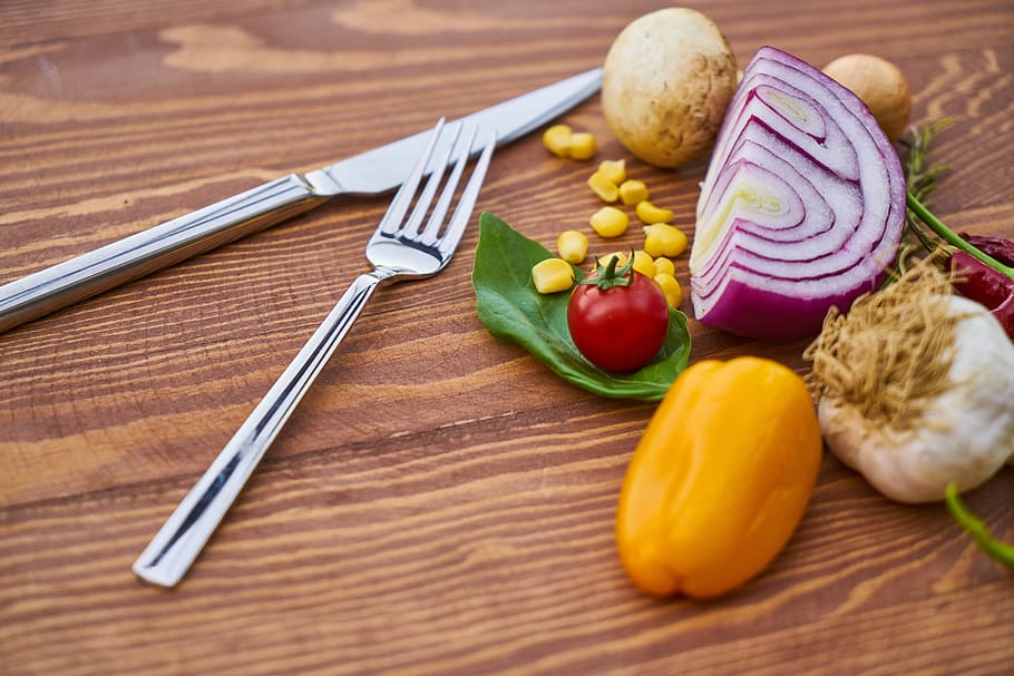 silver metal knife and fork beside vegetables on brown wooden surface