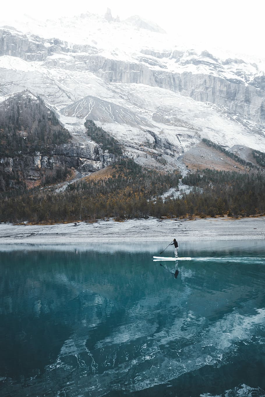 person doing paddle board, person standing on paddle boat on body of water near snow-covered mountains during daytime HD wallpaper