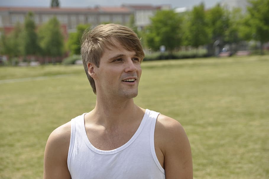 smiling man in white tank top standing on green grass field at daytime HD wallpaper