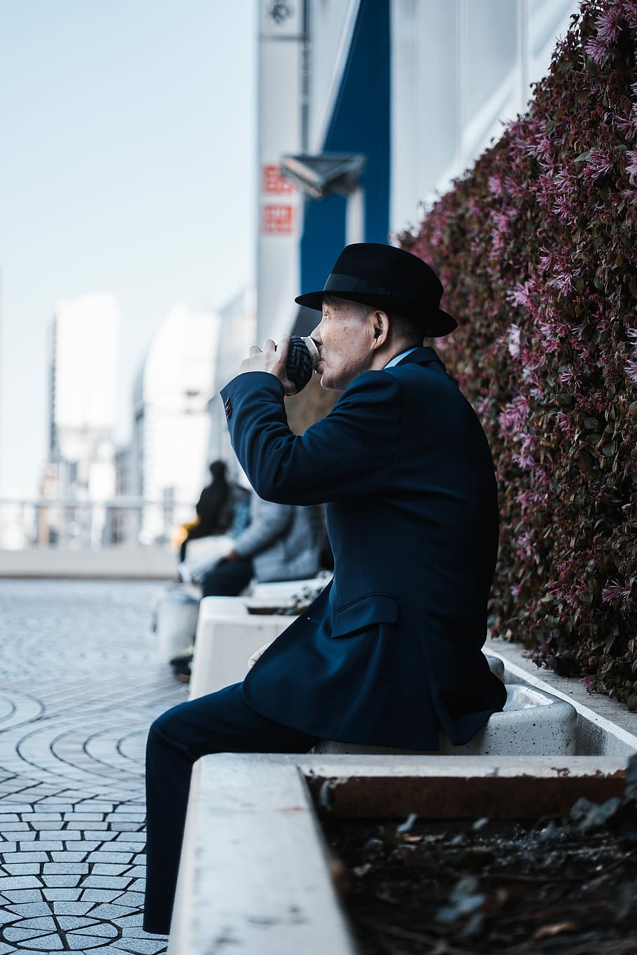 man sitting on chair beside floral wall, selective focus photography of man drinking while sitting HD wallpaper
