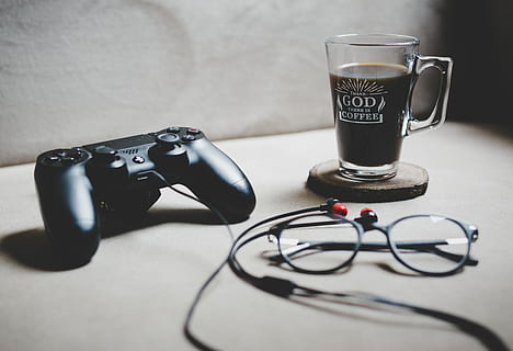 black Sony Dualshock 4 beside clear glass mug filled with coffee, black Sony DualShock 4 HD wallpaper