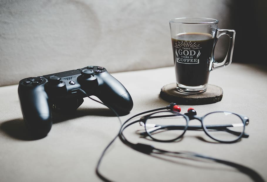 black Sony Dualshock 4 beside clear glass mug filled with coffee, black Sony DualShock 4