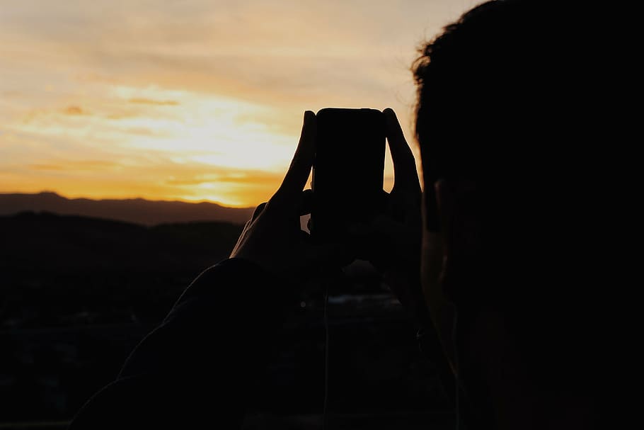 silhouette of person holding phone and taking picture of mountain HD wallpaper