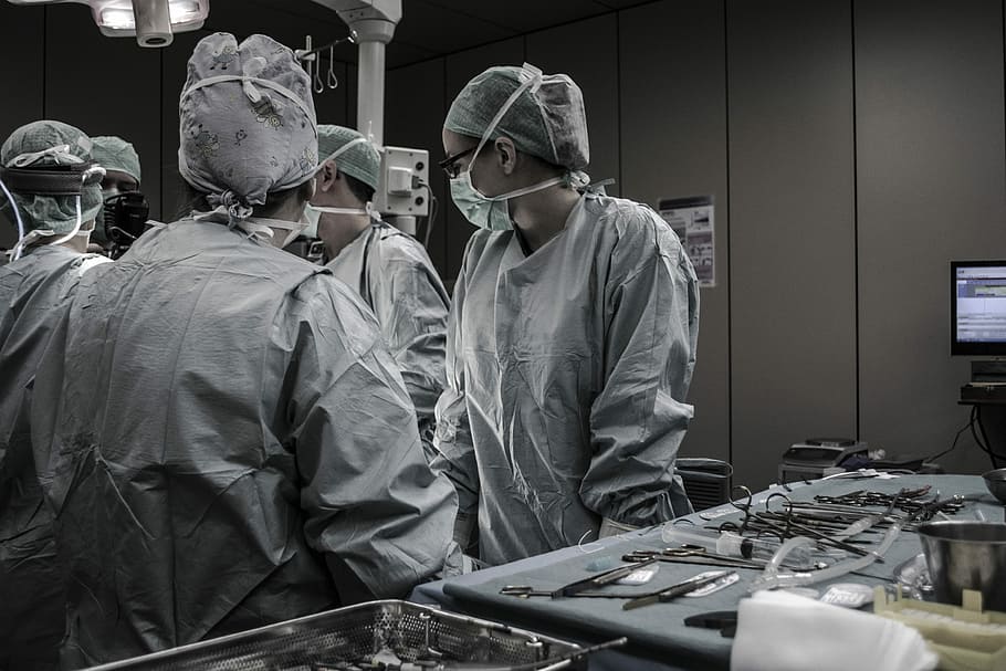medical professionals working, five people wearing masks standing beside tools inside medical room